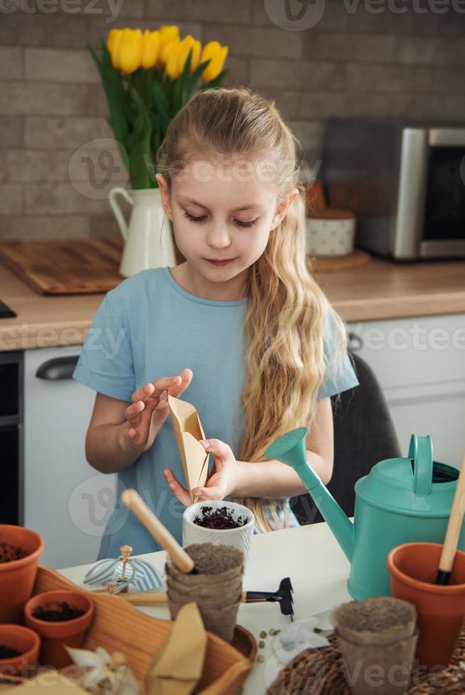 petite fille assise à la table à la maison, semant des graines dans des pots de fleurs. photo