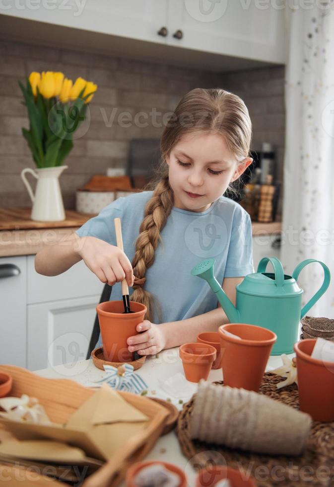 petite fille assise à la table à la maison, semant des graines dans des pots de fleurs. photo