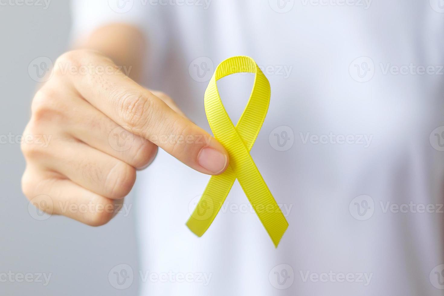 main tenant un ruban jaune pour soutenir les personnes vivant et malades. journée de prévention du suicide de septembre, concept de mois de sensibilisation à l'enfance, au sarcome et au cancer des os photo