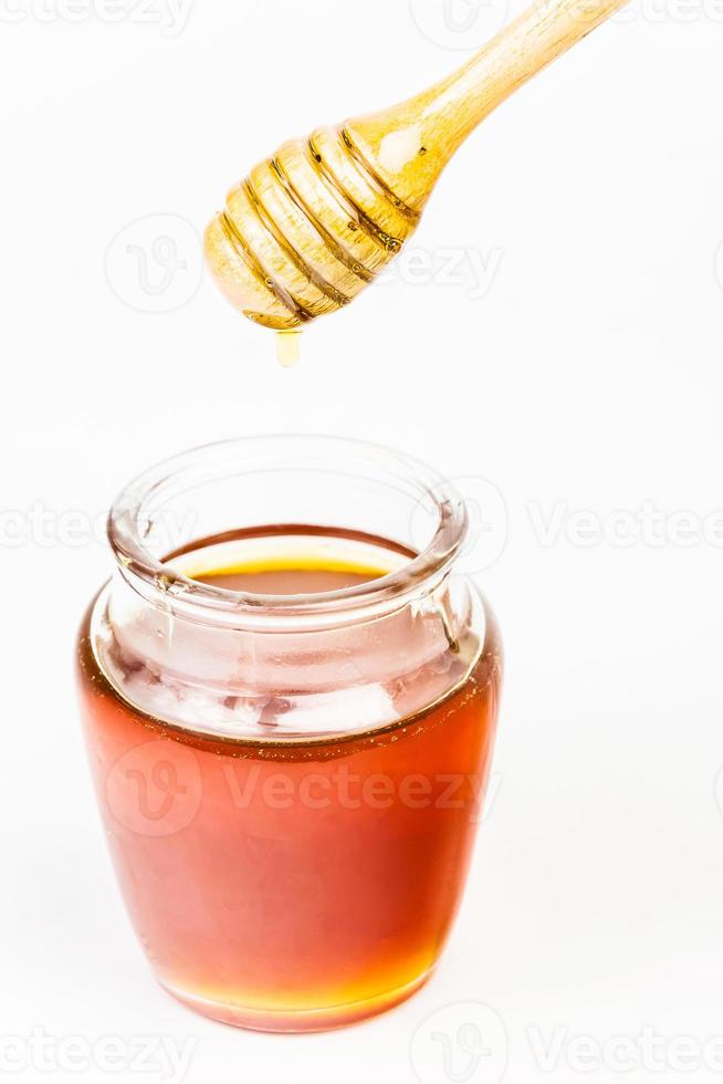 bocal en verre plein de miel balancier miel en bois sur fond blanc photo