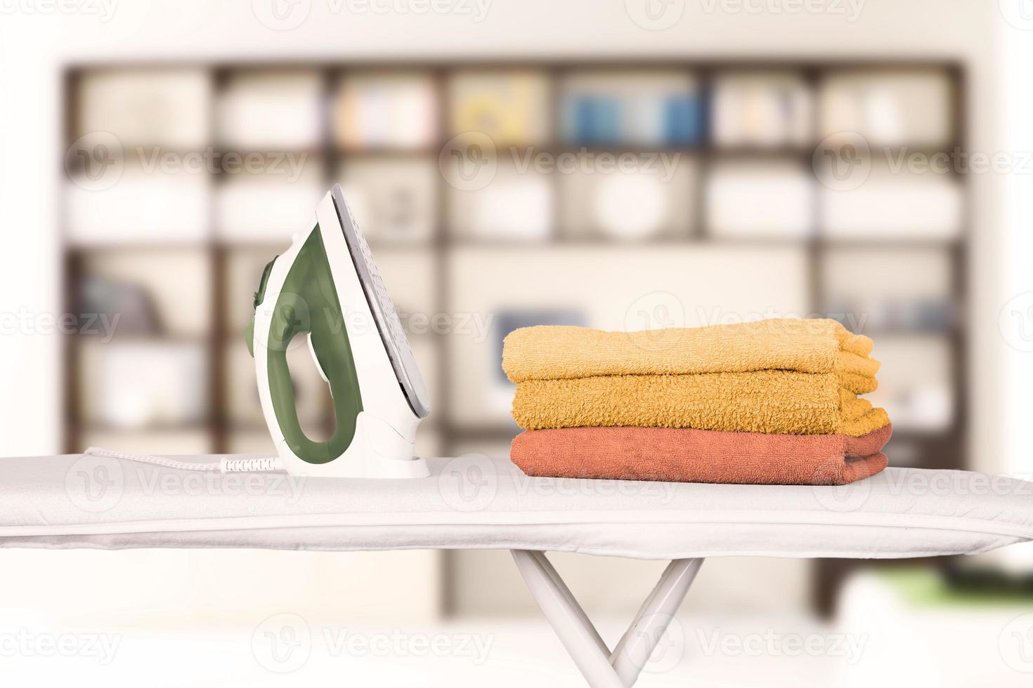 un fer à repasser électrique se dresse sur une planche à repasser et des serviettes de bain pliées en orange et nuances sur le fond d'un intérieur de maison, d'un bureau, d'une bibliothèque. arrière-plan flou, mise au point douce. photo