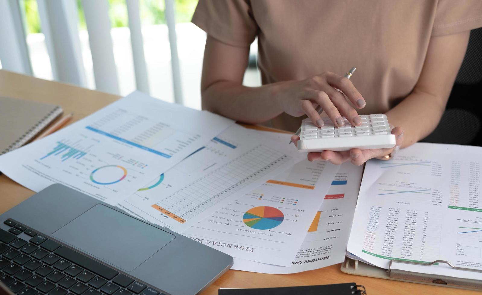 gros plan d'une femme d'affaires ou d'un comptable utilisant une calculatrice pour calculer les données de l'entreprise, travaillant au bureau avec un document papier et un ordinateur portable sur une table de bureau, un concept commercial et financier photo