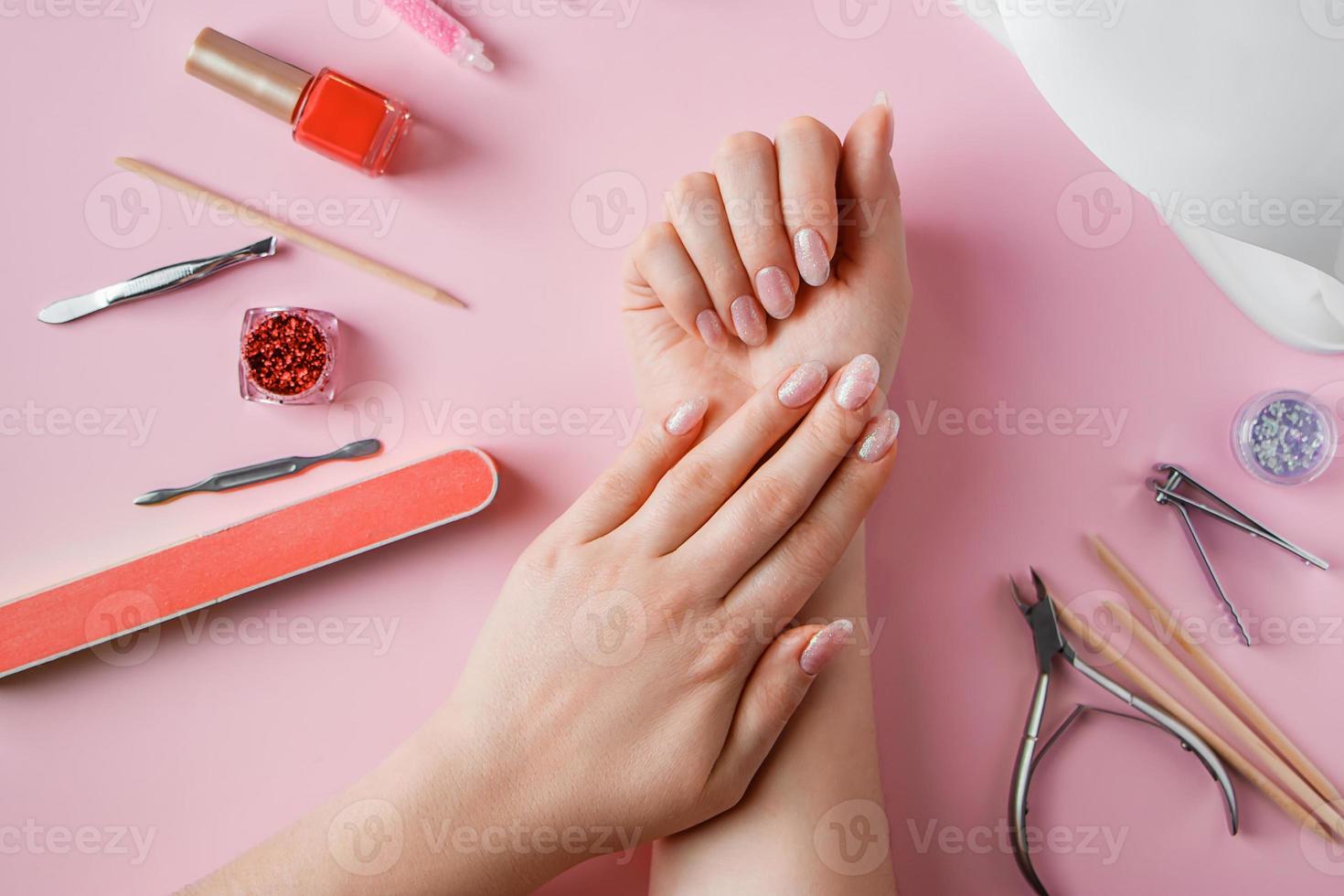 procédure de soin des ongles dans un salon de beauté. mains féminines et outils de manucure sur fond rose. concept spa soins du corps. photo