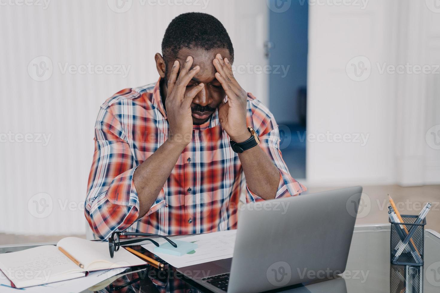 un homme afro-américain épuisé souffre de maux de tête sur un ordinateur portable. stress au travail, épuisement professionnel photo