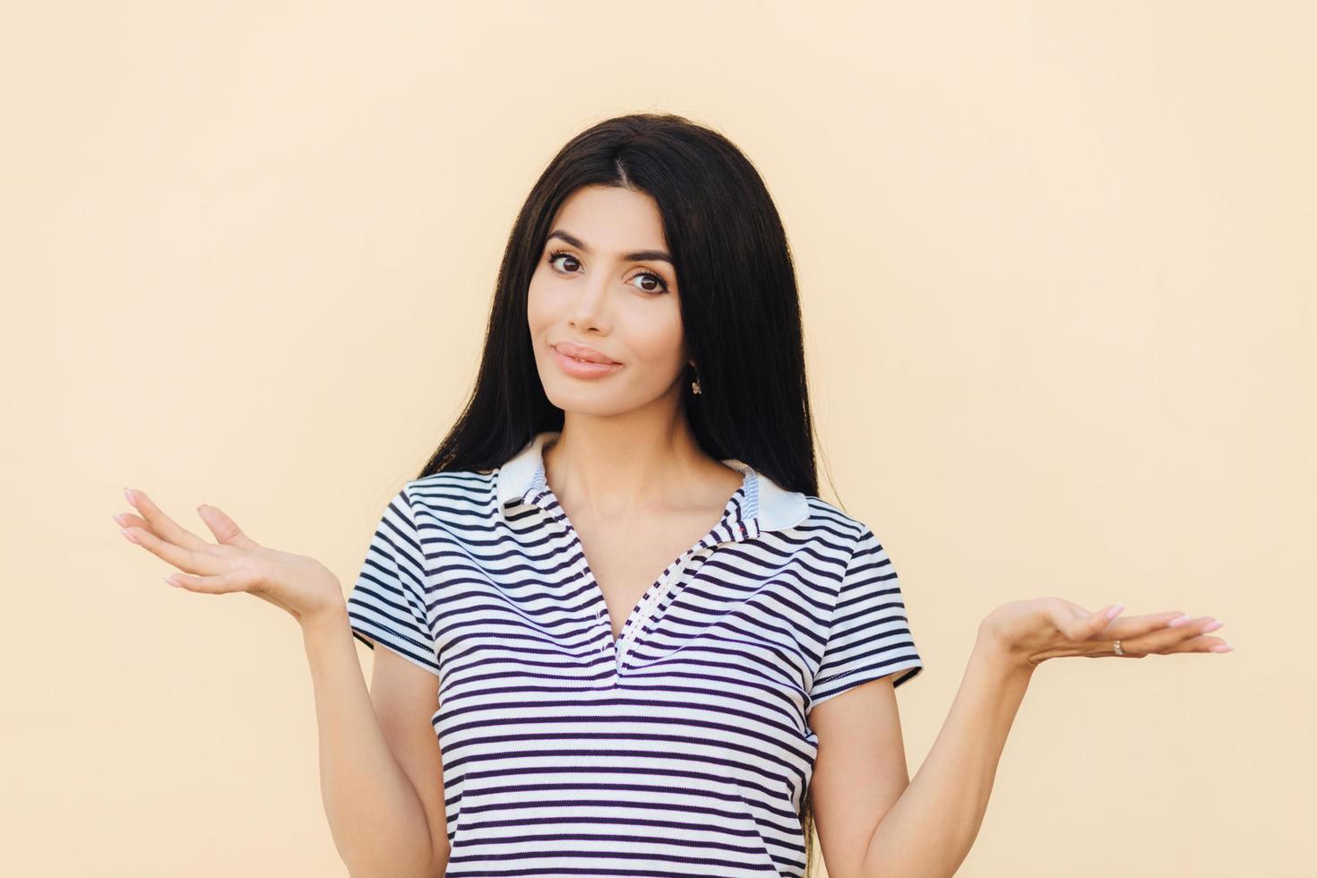 photo d'une jolie femme hésitante qui hausse les épaules avec perplexité, ne sait pas répondre à une question difficile, pose sur fond rose clair. Une femme brune désemparée a une expression douteuse