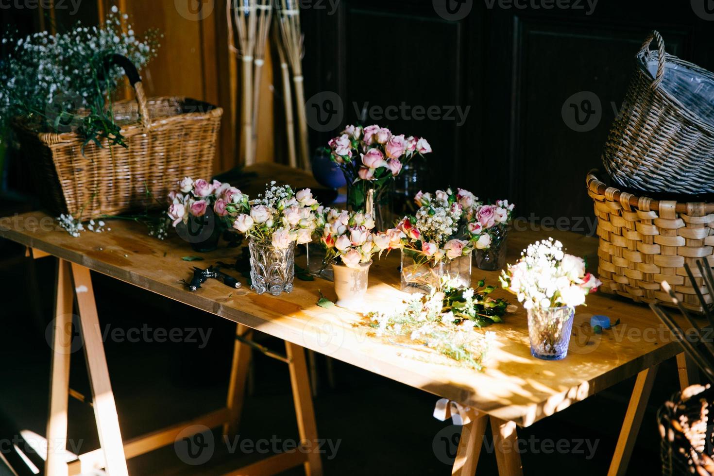 longue table en bois avec différents bouquets de belles fleurs. roses odorantes agréables debout dans des verres. supports en bois vides. création de bouquet de fleurs. roses arrangées pour la décoration photo