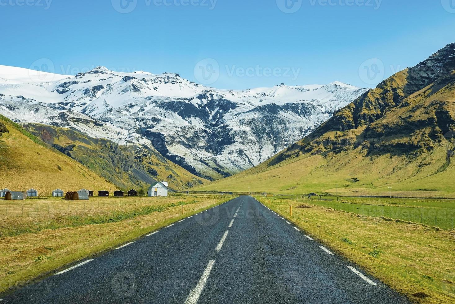 Diminution de la route vide menant vers la montagne enneigée contre le ciel bleu clair photo