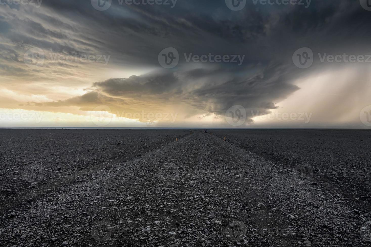 voie vide sur le sable de lave à la plage noire contre le ciel dramatique pendant le coucher du soleil photo