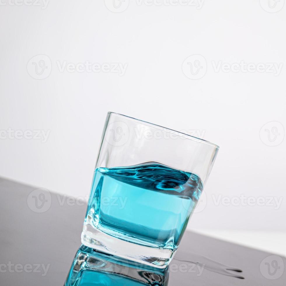 verre pour liqueur mettre un liquide bleu en verre posé sur une table inclinée fond blanc photo