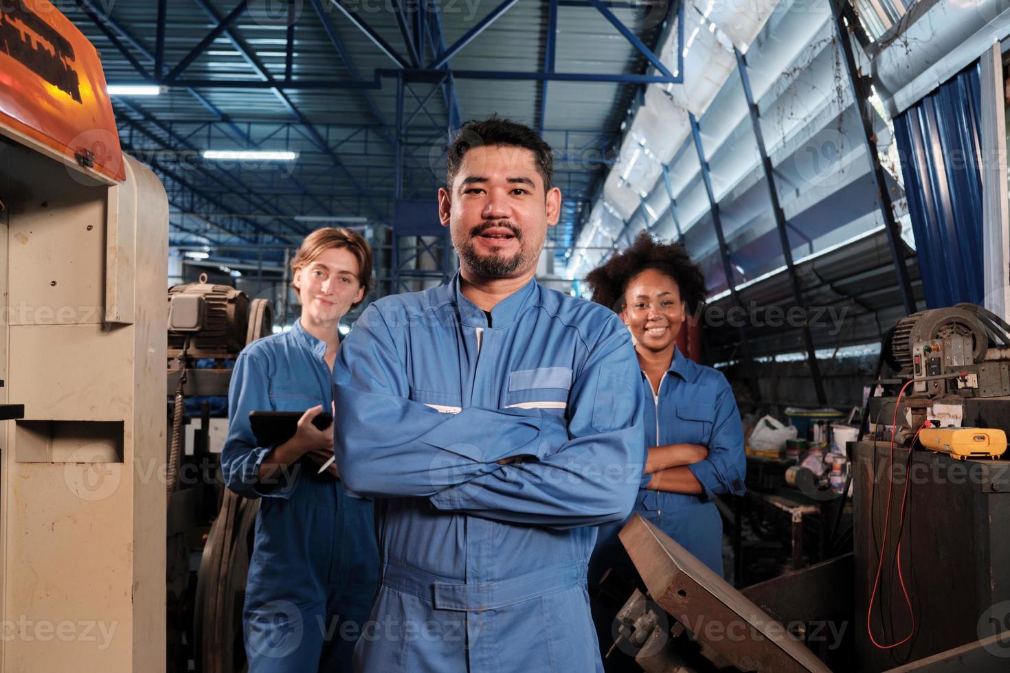 les travailleurs de l'industrie multiraciale en uniformes de sécurité collaborent avec l'unité, les bras croisés et expriment un travail heureux avec le sourire et la joie dans une usine mécanique, profession d'ingénieur professionnel. photo