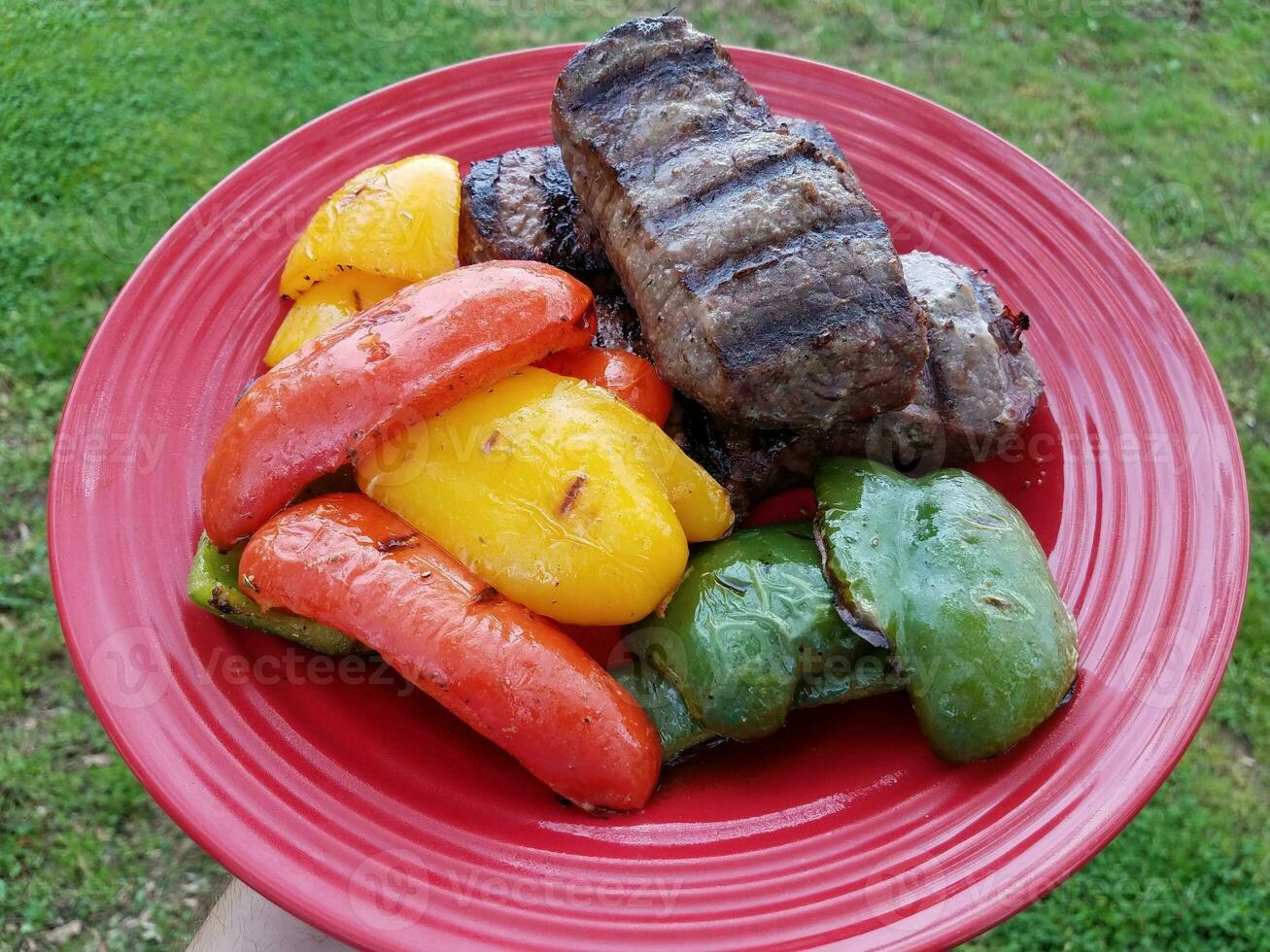 main tenant une assiette rouge avec steak grillé et poivrons rouges jaunes et verts photo