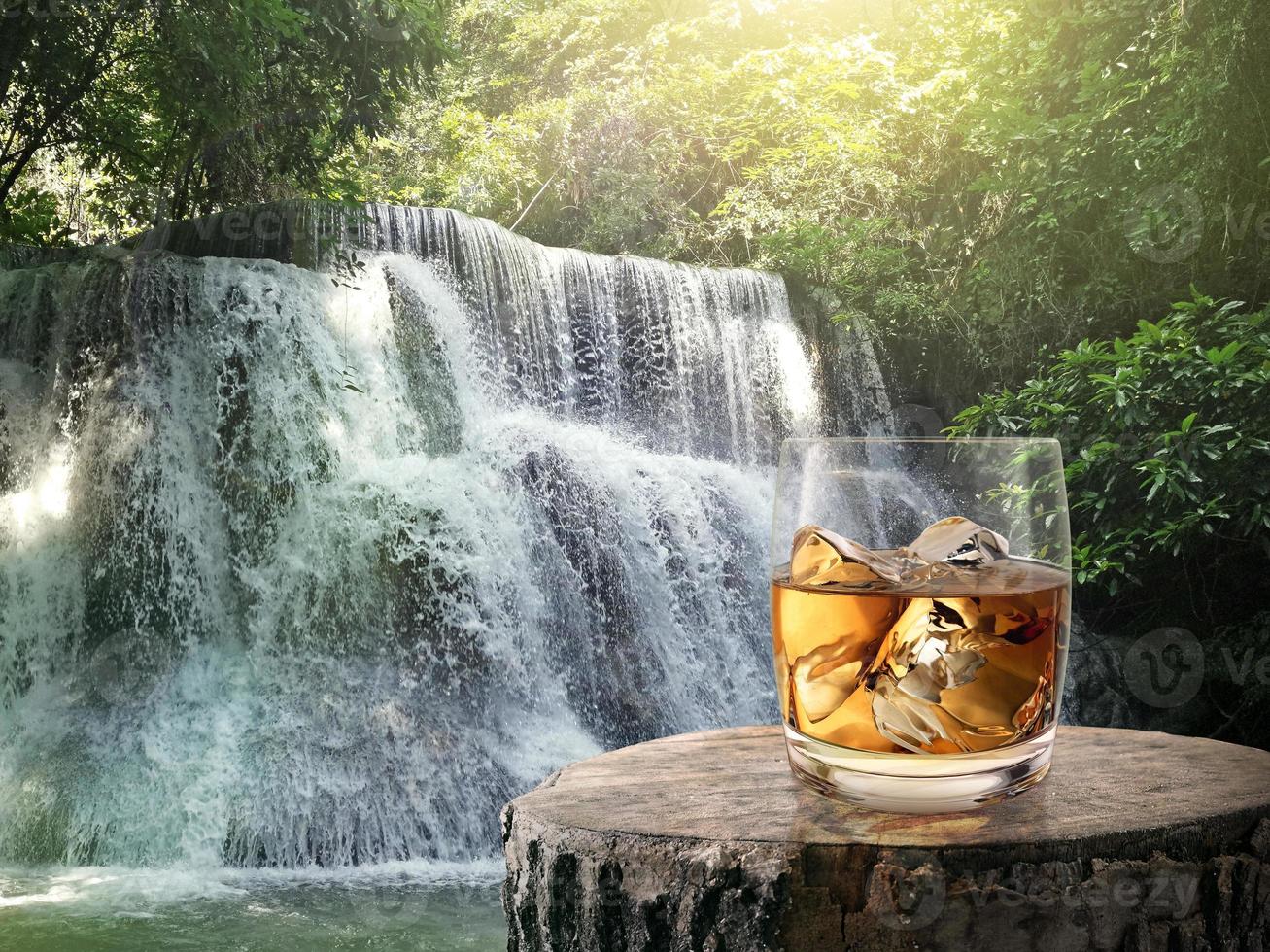 verre de whisky, sur la bûche de bois et le fond de la cascade du matin photo