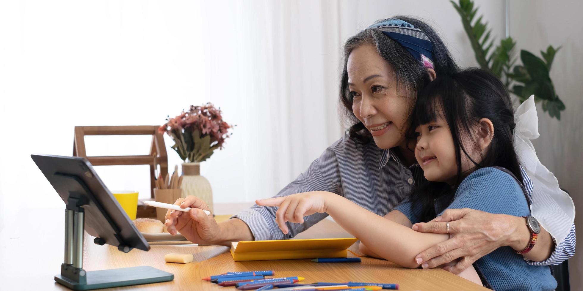 grand-mère aimante étreinte les épaules d'une petite fille petit-enfant aider à préparer le soutien aux devoirs donner des conseils. Sympathique femme âgée enseignant regardant petit enfant élève écrivant la solution du problème de mathématiques photo