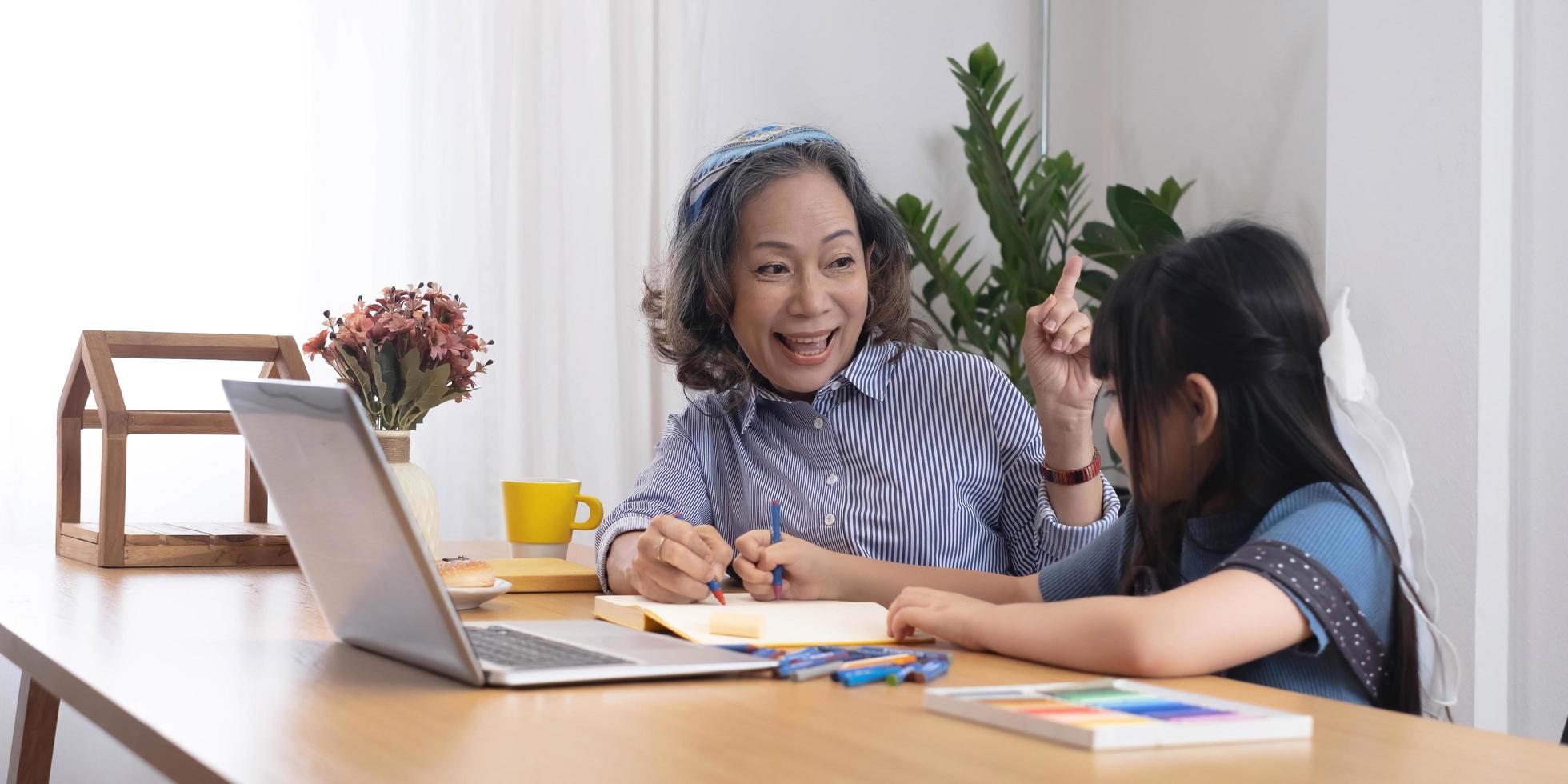 une grand-mère asiatique enseigne à sa petite-fille à dessiner et à faire ses devoirs à la maison. photo