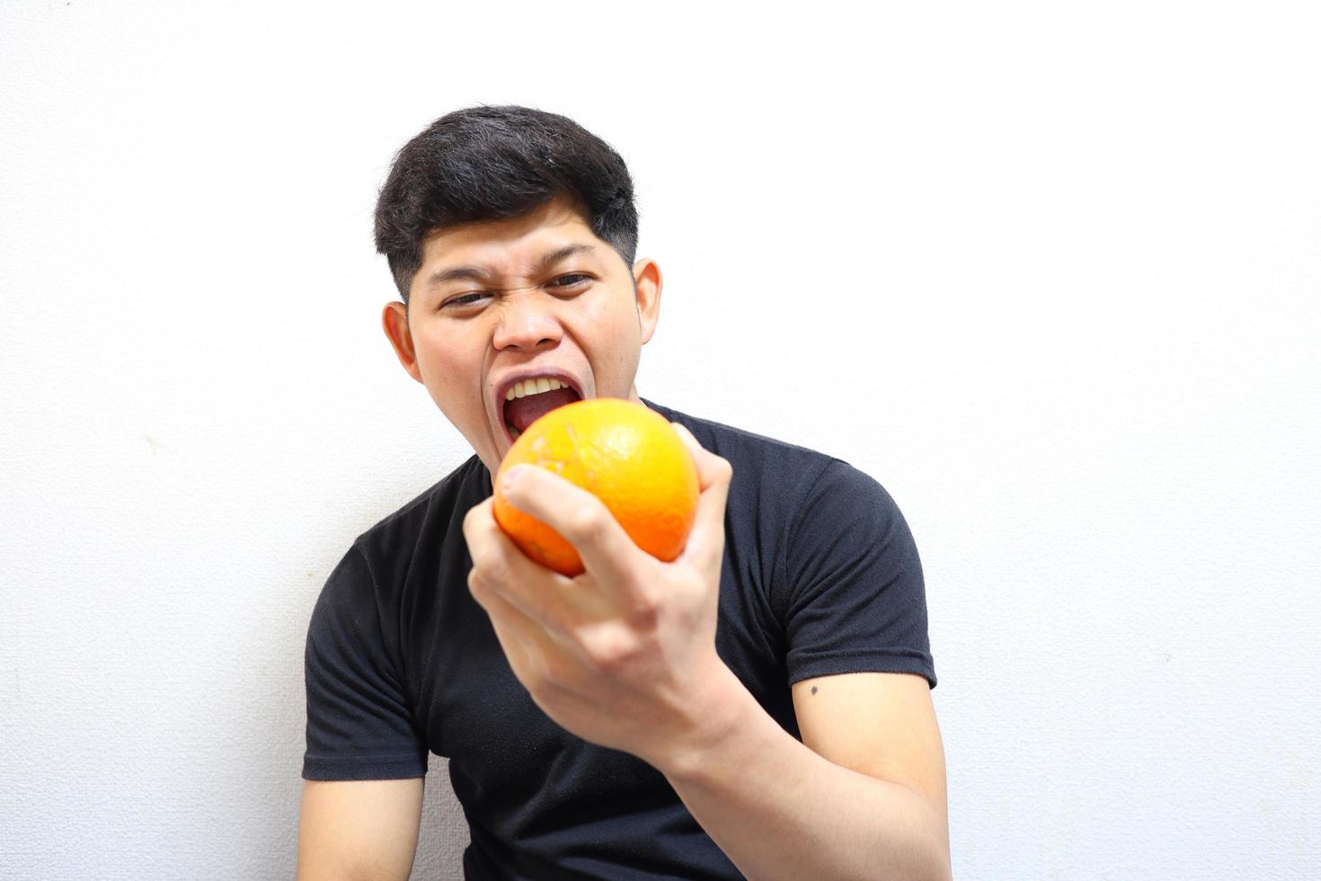 homme asiatique séduisant mangeant des oranges. isolé sur fond blanc photo