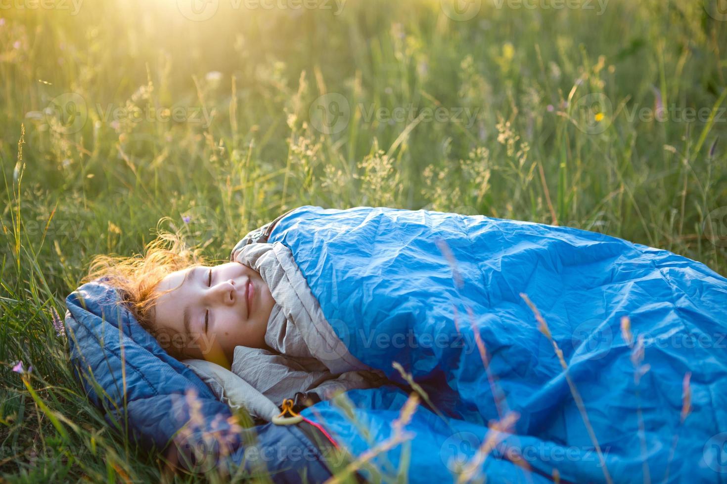 un enfant dort dans un sac de couchage sur l'herbe lors d'un voyage de camping - loisirs de plein air respectueux de l'environnement, mode de vie sain, heure d'été. sommeil doux et paisible. piqûres de moustiques, répulsif. photo