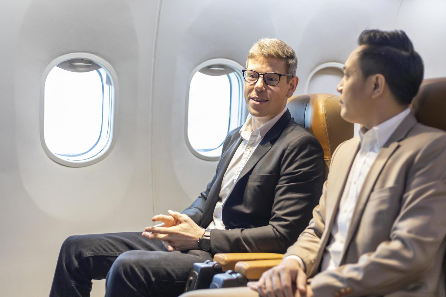 homme d'affaires caucasien voyage en tenue de soirée et son partenaire assis confortablement dans l'avion avec siège en classe affaires avec espace de copie photo