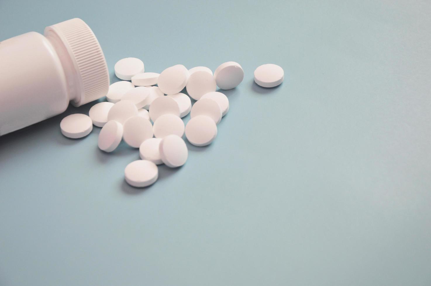 pot en plastique blanc avec médicament et pilules blanches dispersées sur fond bleu. notion de soins de santé. espace libre pour le texte. photo