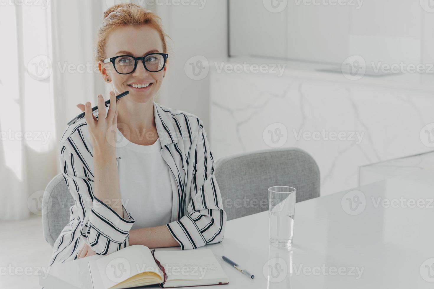 jeune femme d'affaires souriante utilisant l'application d'assistant vocal sur smartphone, assise à table à la maison photo