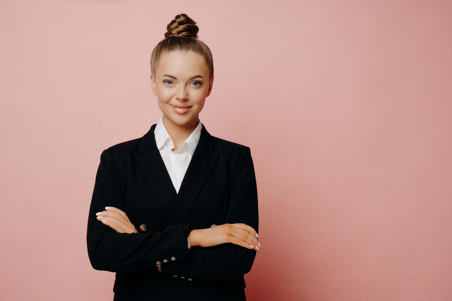 Confiant femme employée de bureau avec des cheveux en chignon posant isolé sur fond rose photo