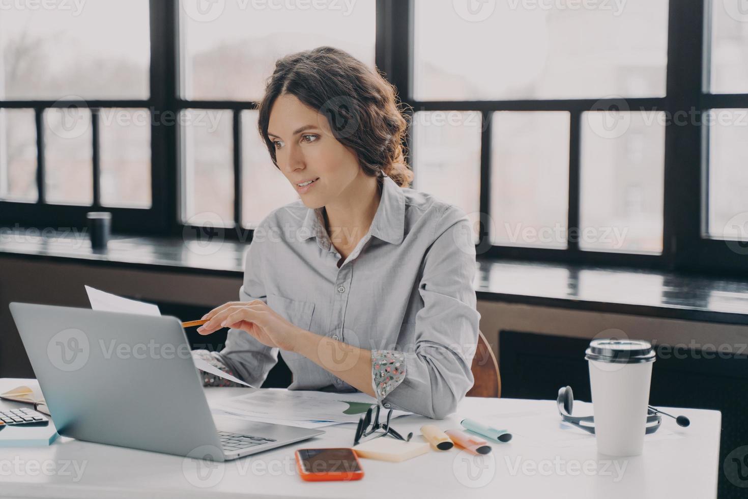 jeune femme d'affaires européenne prospère en tenue de soirée analysant des documents au travail photo