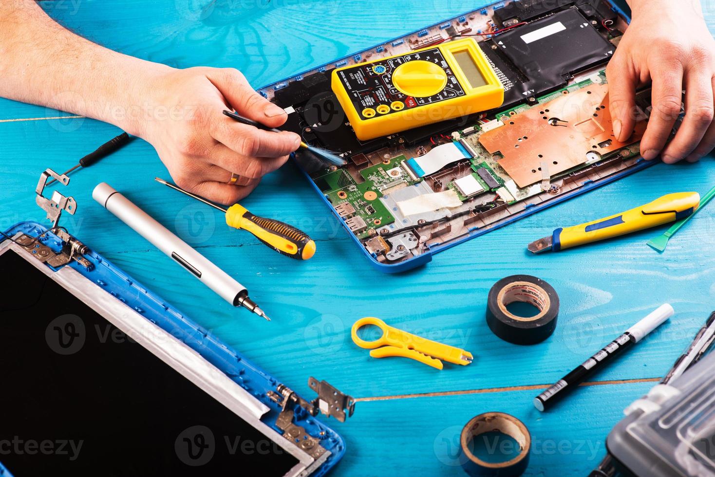 l'assistant répare l'ordinateur portable avec des outils et des mains sur la table en bois bleue. vue de dessus photo