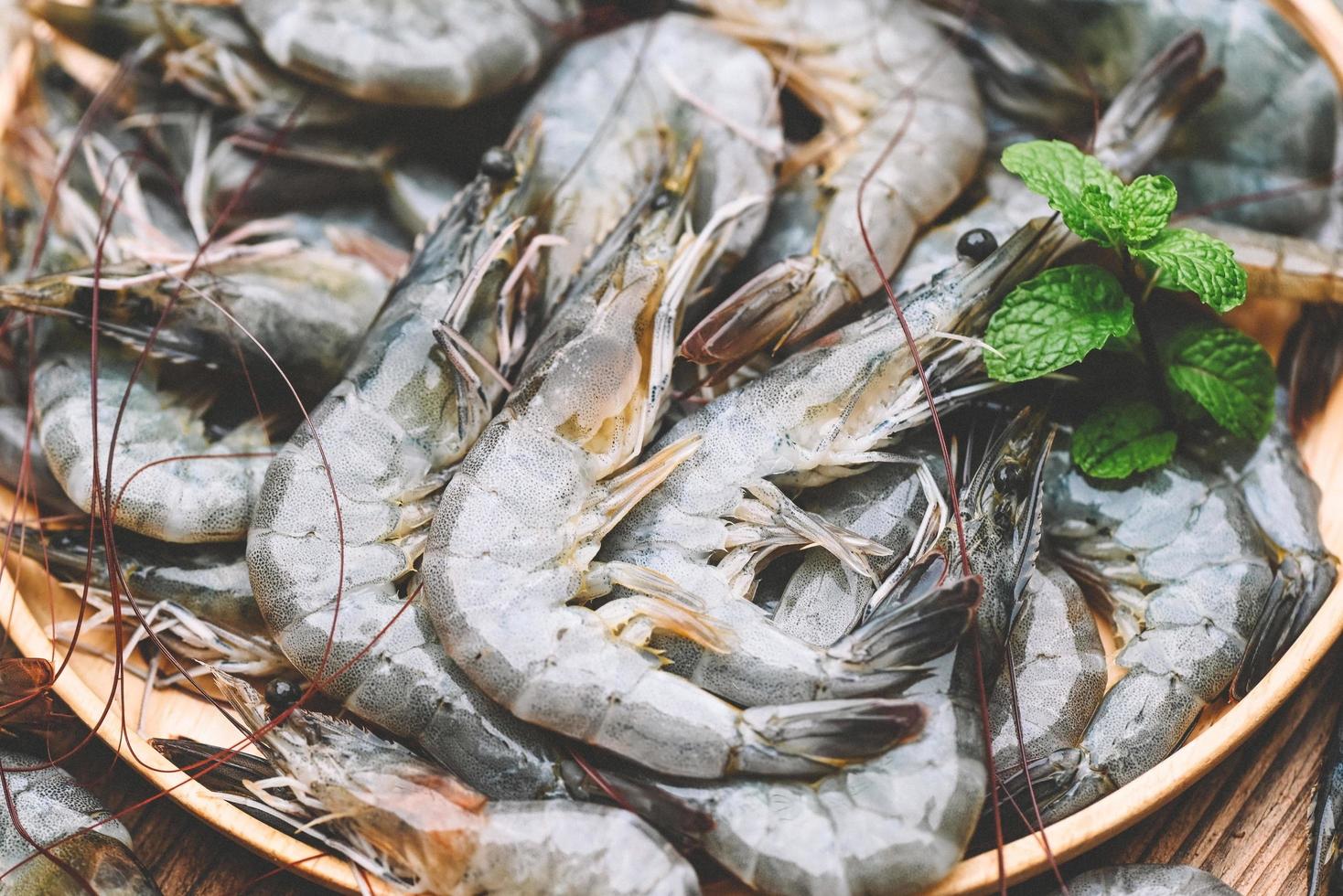 crevettes crues sur plaque blanche avec feuille de menthe et fond de crevettes pour la cuisson, gros plan de crevettes ou de crevettes fraîches, fruits de mer photo