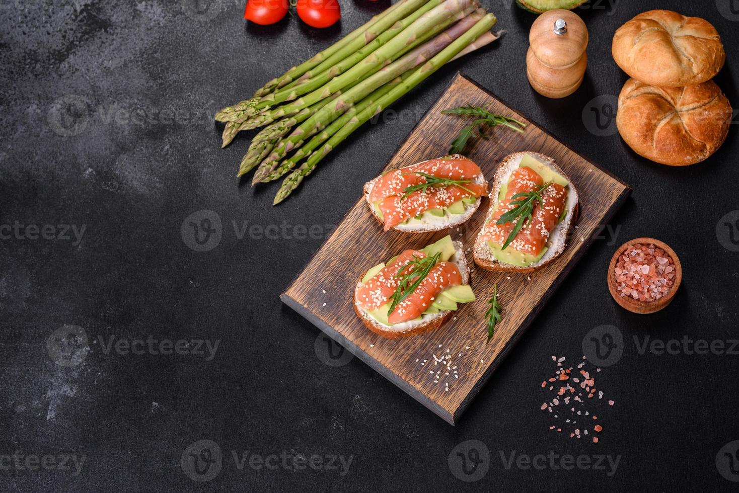 sandwich toast au beurre, avocat et saumon, décoré de roquette et de graines de sésame, sur fond de pierre noire photo