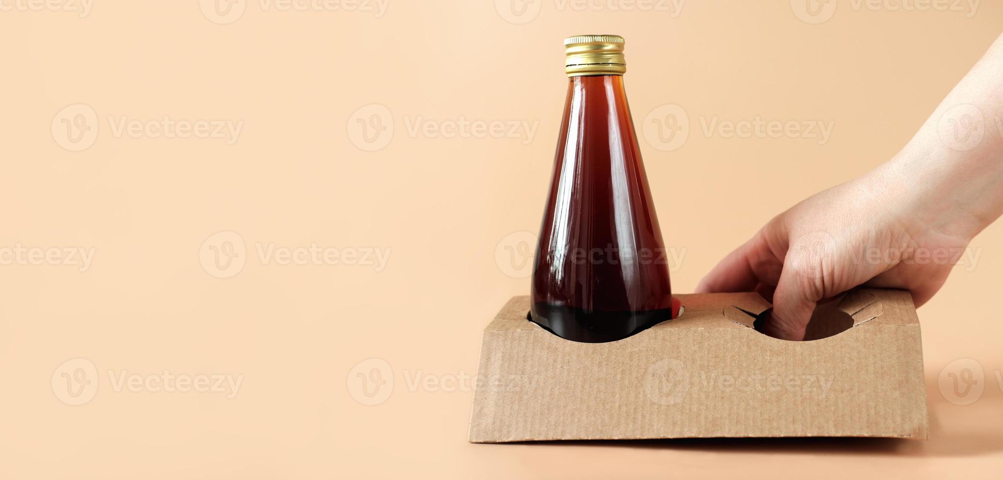 café infusé à froid dans une bouteille en verre. concept de café à emporter. main tenant un carton ou un support biodégradable en papier, emballage écologique pour les boissons de tous les jours, bannière photo