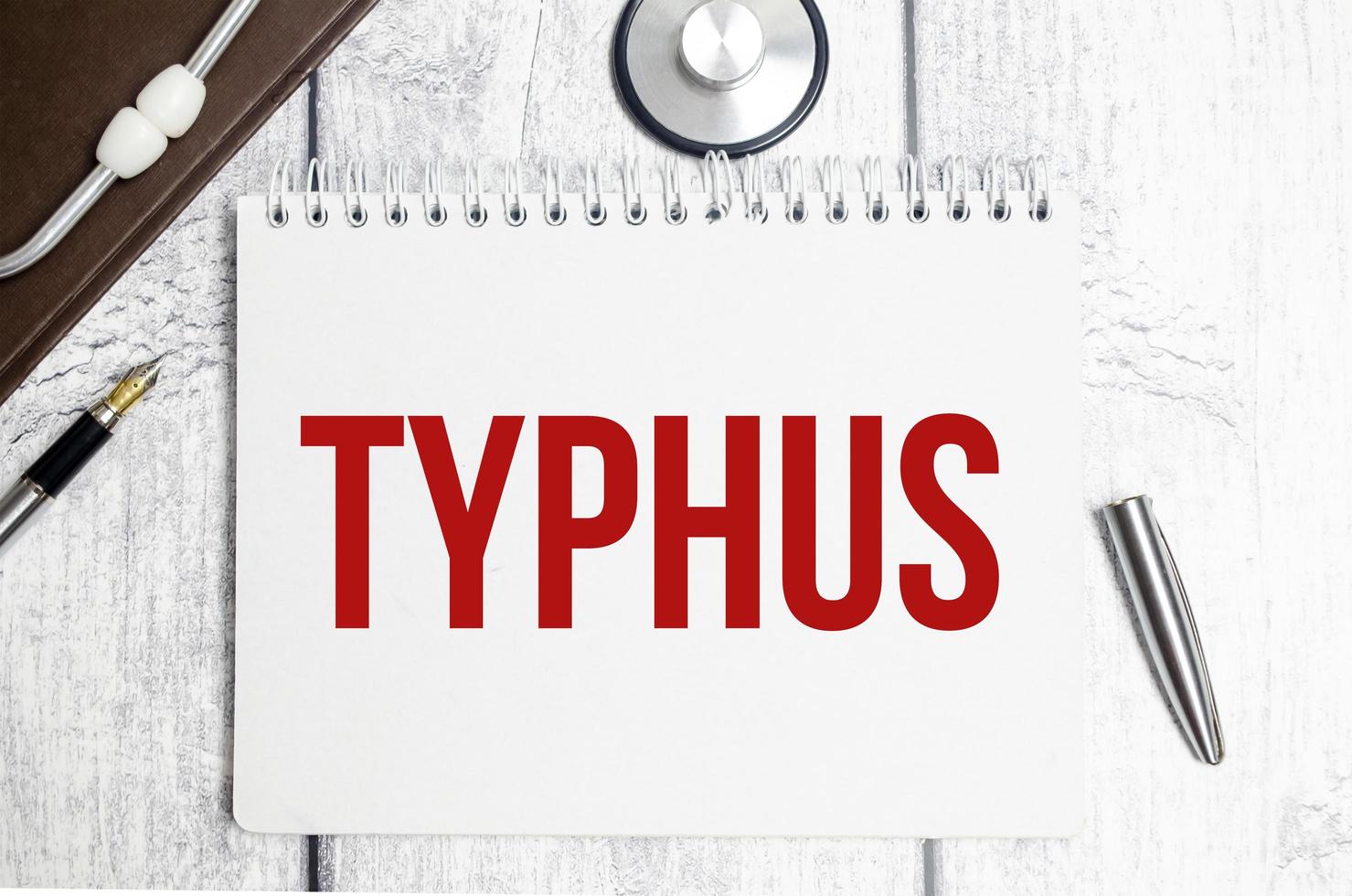 mot typhus sur cahier blanc et stylo avec stéthoscope photo