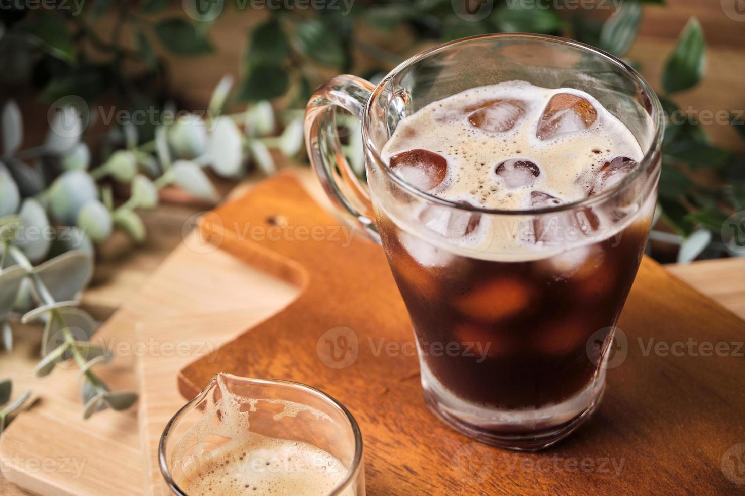 café noir glacé froid dans un verre avec des morceaux de glace sur une table en bois, lumière naturelle, boisson fraîche d'été le matin photo