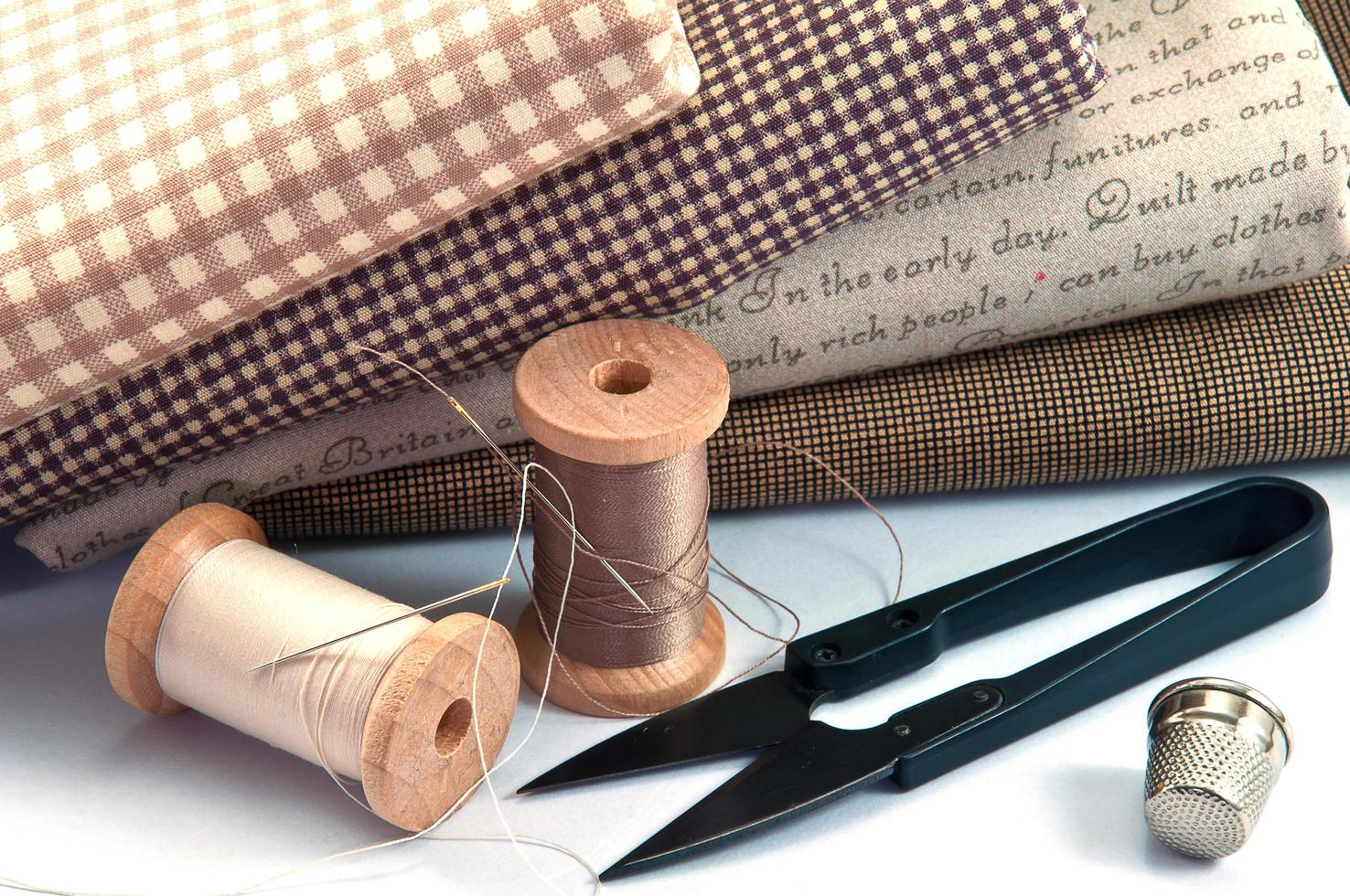 accessoire de couture comprenant bobine de fil, aiguille, ciseaux, dé à coudre et tissu sur fond blanc photo