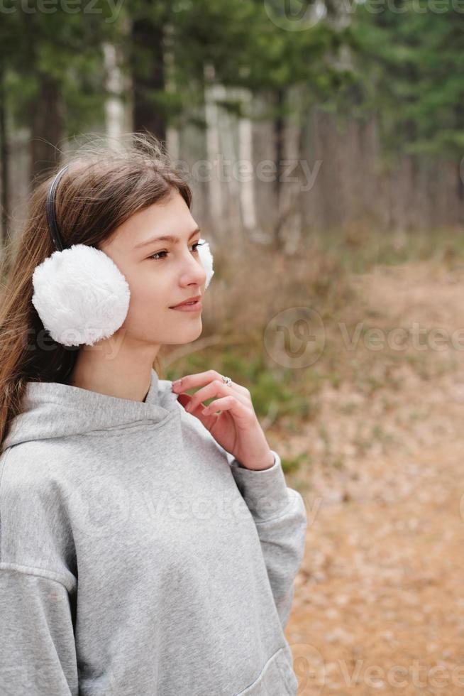 portrait en plein air d'une adolescente portant des cache-oreilles blancs. fille marchant dans la forêt. adolescent regardant de côté. randonnée et suivi seul. concept de voyage local photo