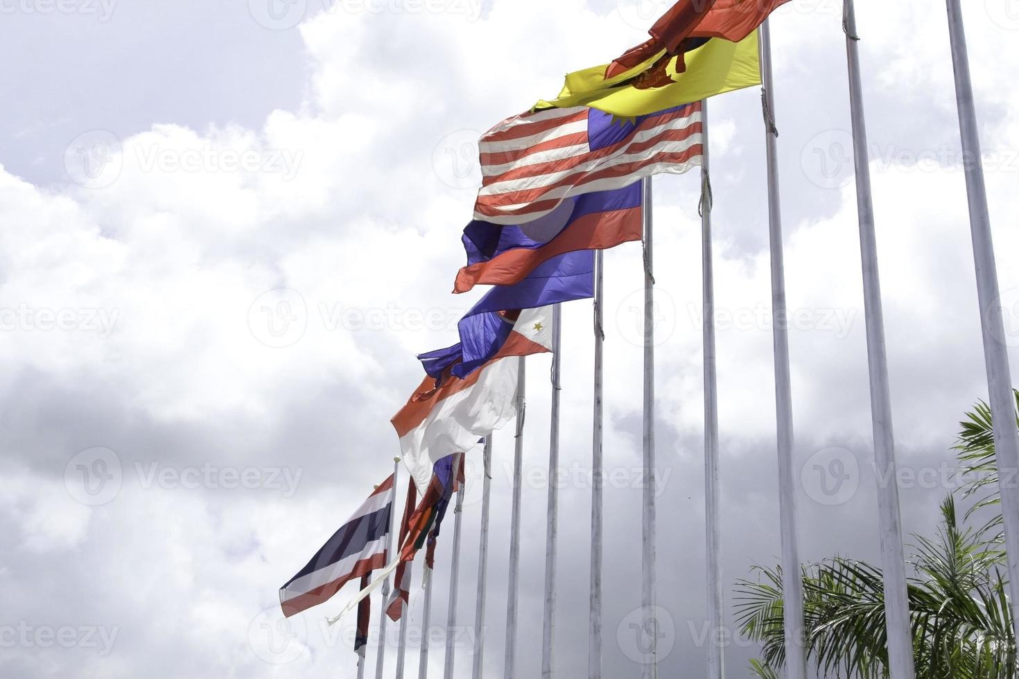 de nombreux drapeaux de l'asean aux couleurs colorées soufflés par la force du vent flottant sur un poteau devant un hôtel en thaïlande sur fond de nuages et de ciel bleu. photo
