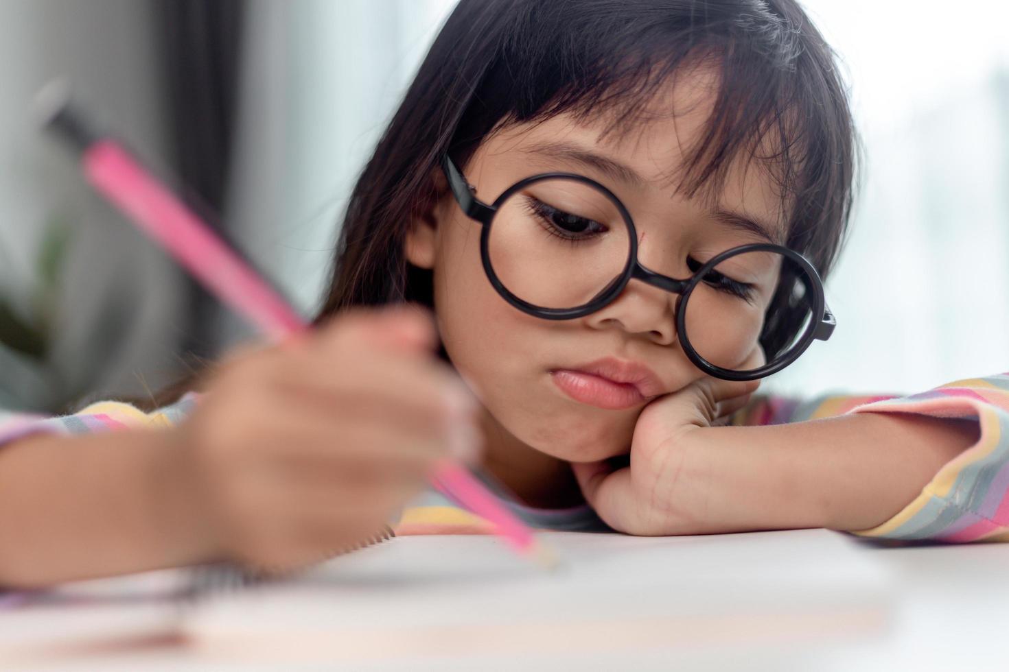 petite fille asiatique assise seule et regardant dehors avec un visage ennuyé, enfant d'âge préscolaire allongé sur la table avec triste ennuyé par les devoirs, enfant gâté photo