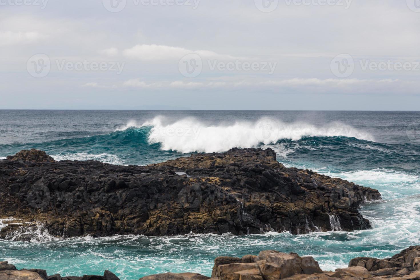 les vagues océaniques turbulentes avec de la mousse blanche battent les pierres côtières photo