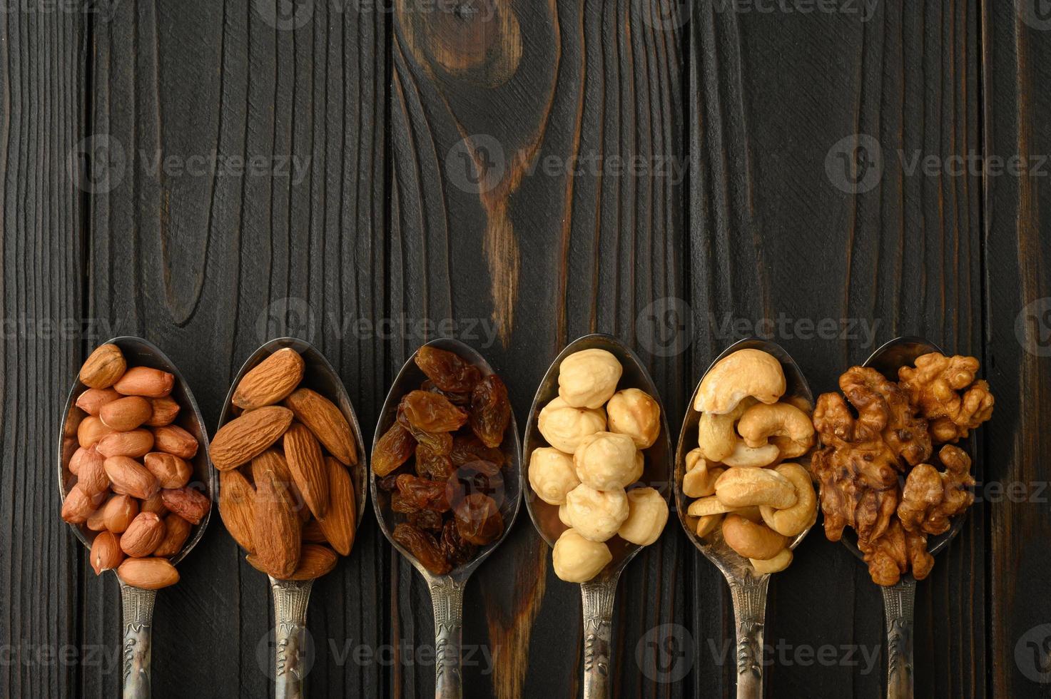 noisette, noix de cajou, raisins secs, amandes, cacahuètes, noix dans des cuillères en argent sur fond rustique photo