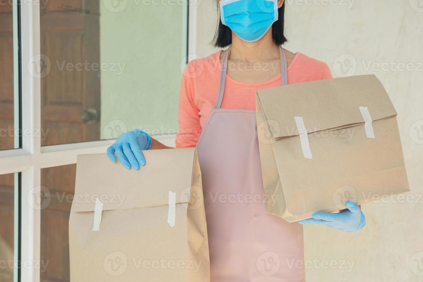 facteur, livreur portant un masque porte une petite boîte livrée au client devant la porte à la maison. une femme portant un masque prévient le covid 19, l'épidémie d'infection à coronavirus. concept de livraison à domicile. photo