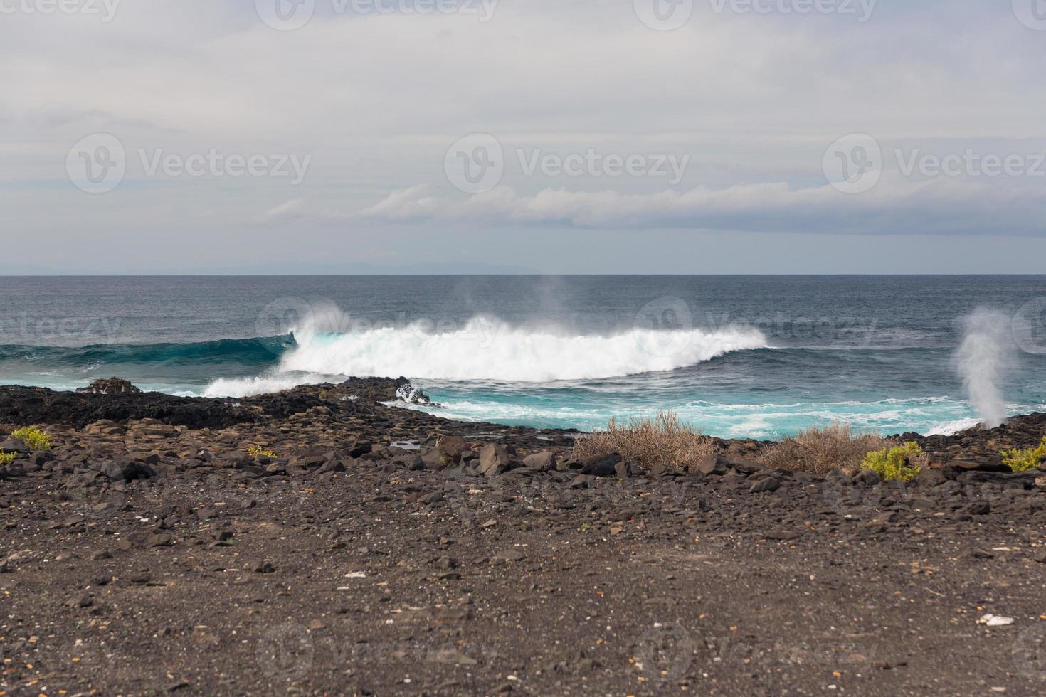 les vagues océaniques turbulentes avec de la mousse blanche battent les pierres côtières photo