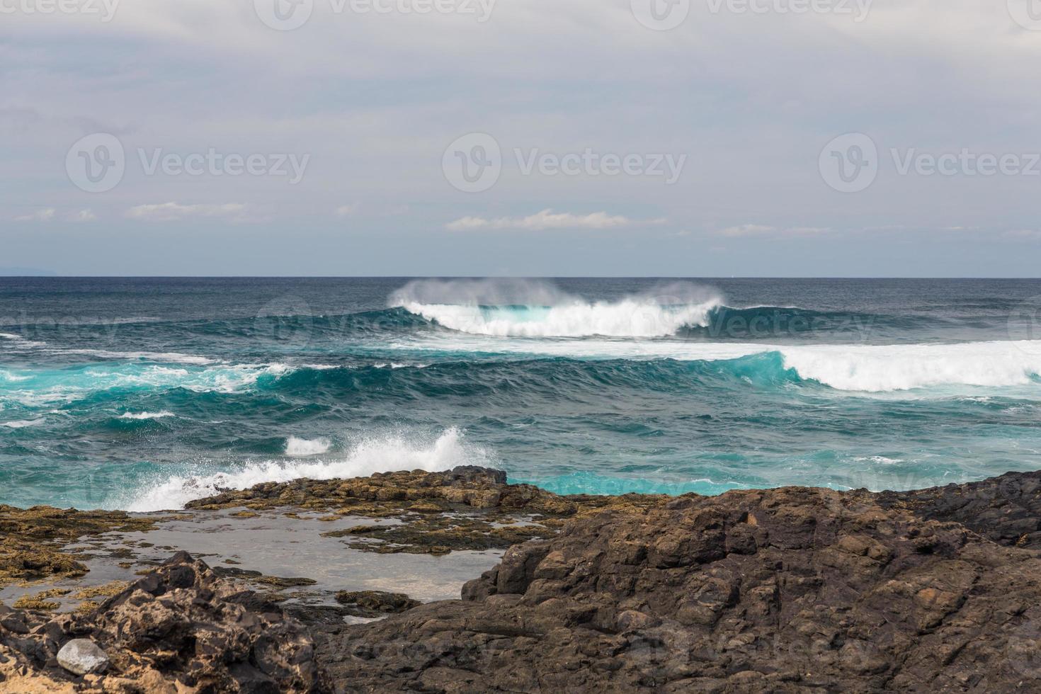 les vagues océaniques turbulentes avec de la mousse blanche battent les pierres côtières photo