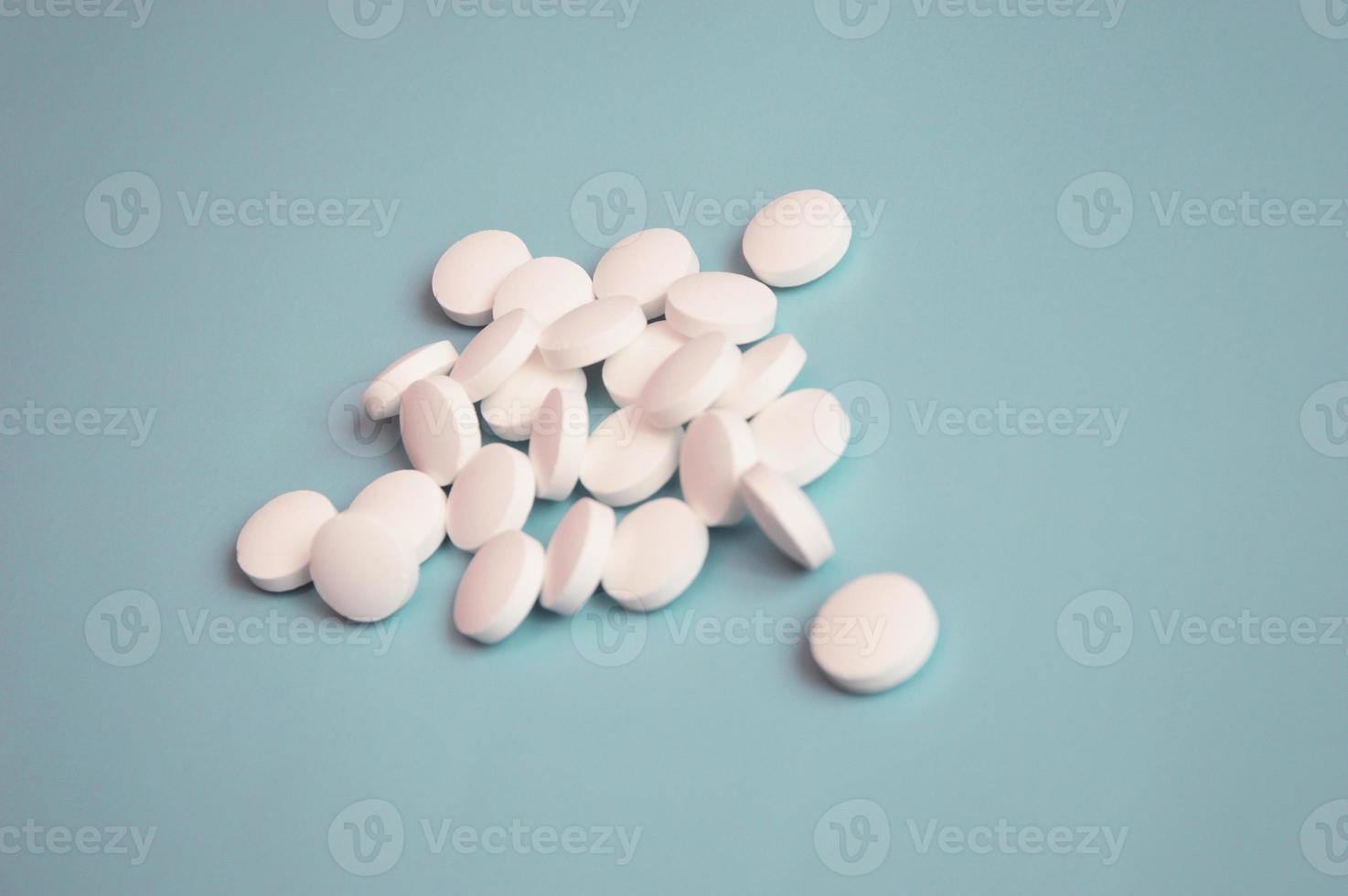 des pilules médicales blanches en vrac se trouvent sur un fond turquoise clair. notion de soins de santé. médicaments, bioadditifs. industrie pharmaceutique. photo