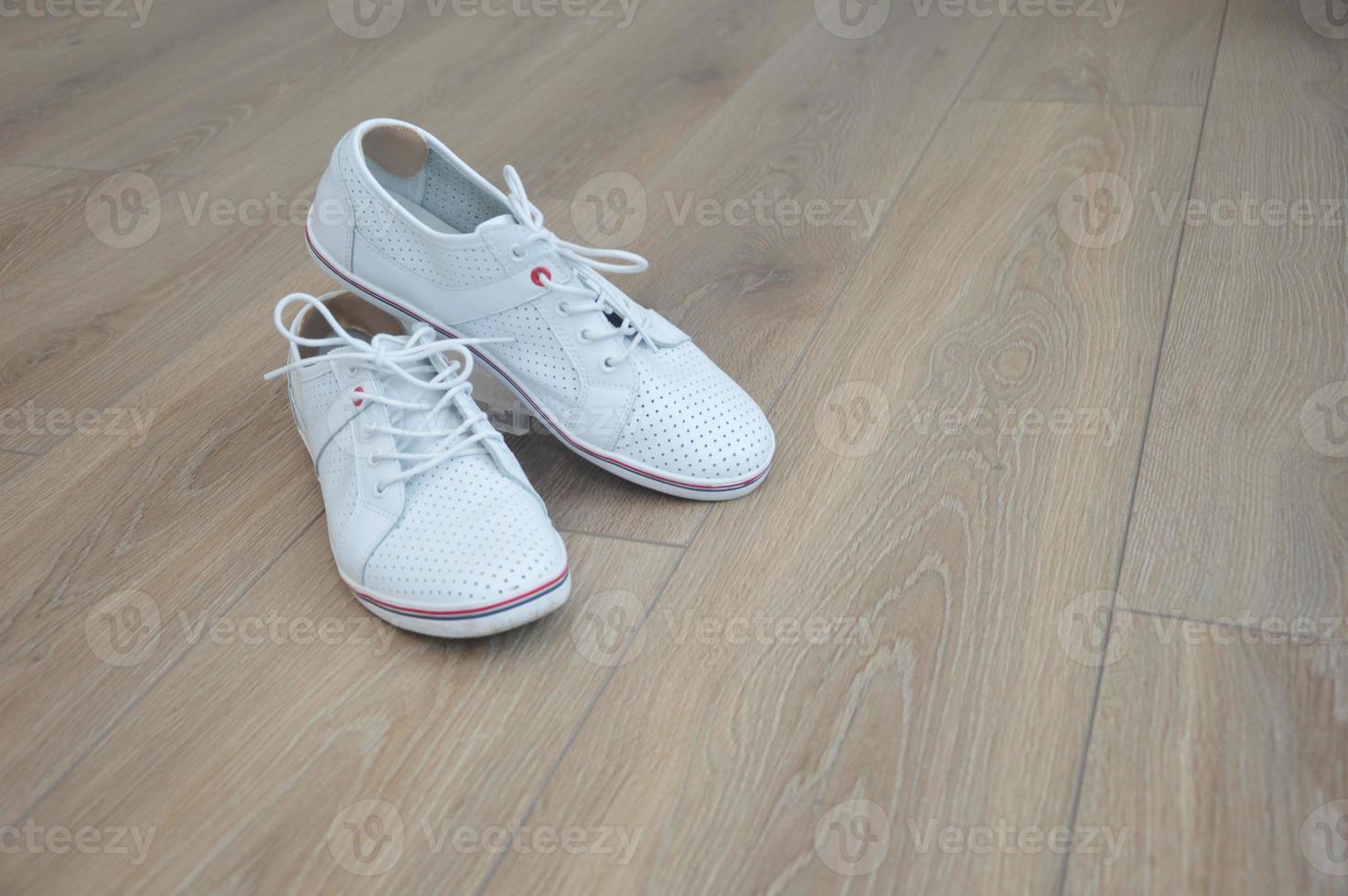 baskets en cuir blanc sur un sol en bois marron. inserts souples du frottement des cors sur les talons. chaussures de mode. place pour le texte. photo