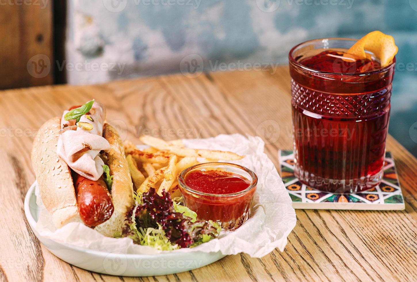 assiette avec hot-dog avec saucisse et jambon, ketchup à la sauce tomate et cocktail français frit à l'ancienne et sur la table du bar photo