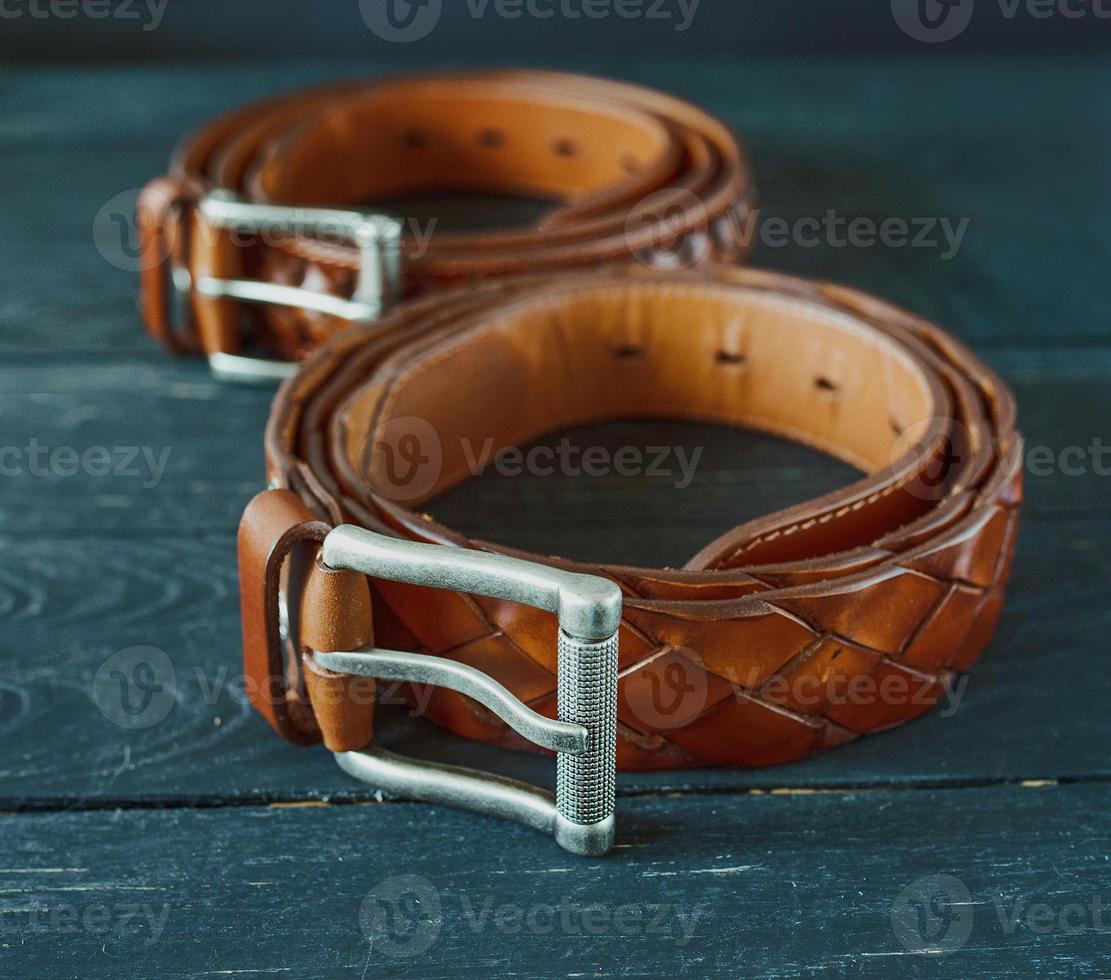 Deux ceintures en cuir marron foncé sur fond de bois photo