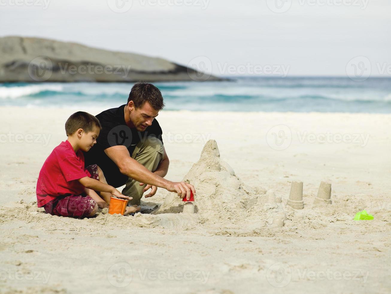 père et fils construisant des châteaux de sable sur la plage. photo