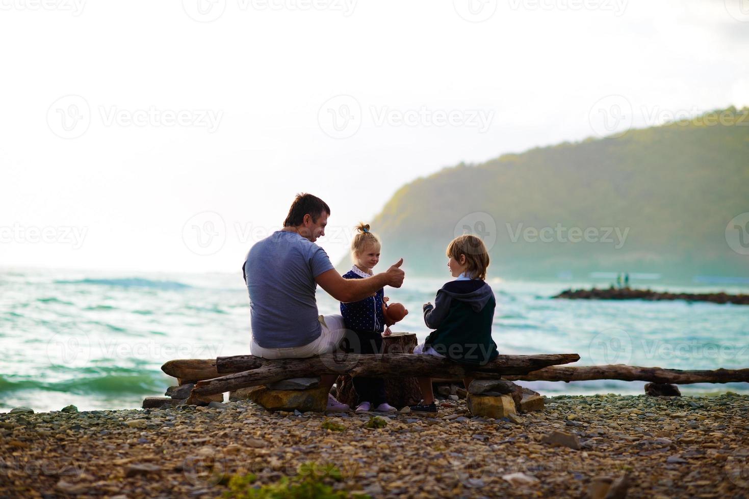père assis avec ses enfants sur la plage photo