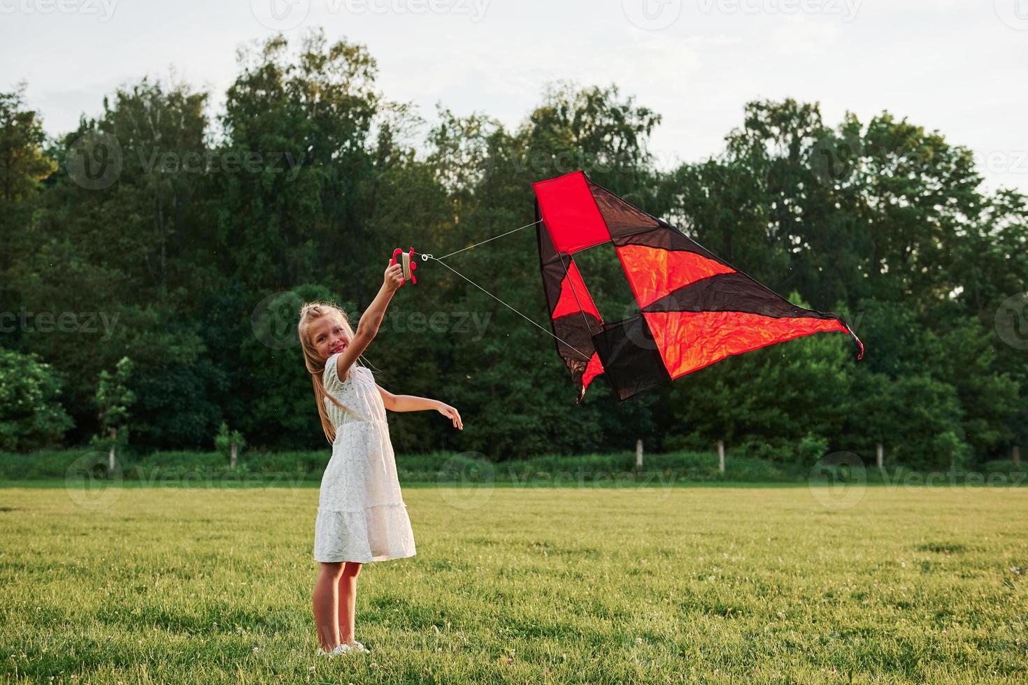 Regardez-moi. une fille heureuse en vêtements blancs s'amuse avec un cerf-volant sur le terrain. belle nature photo