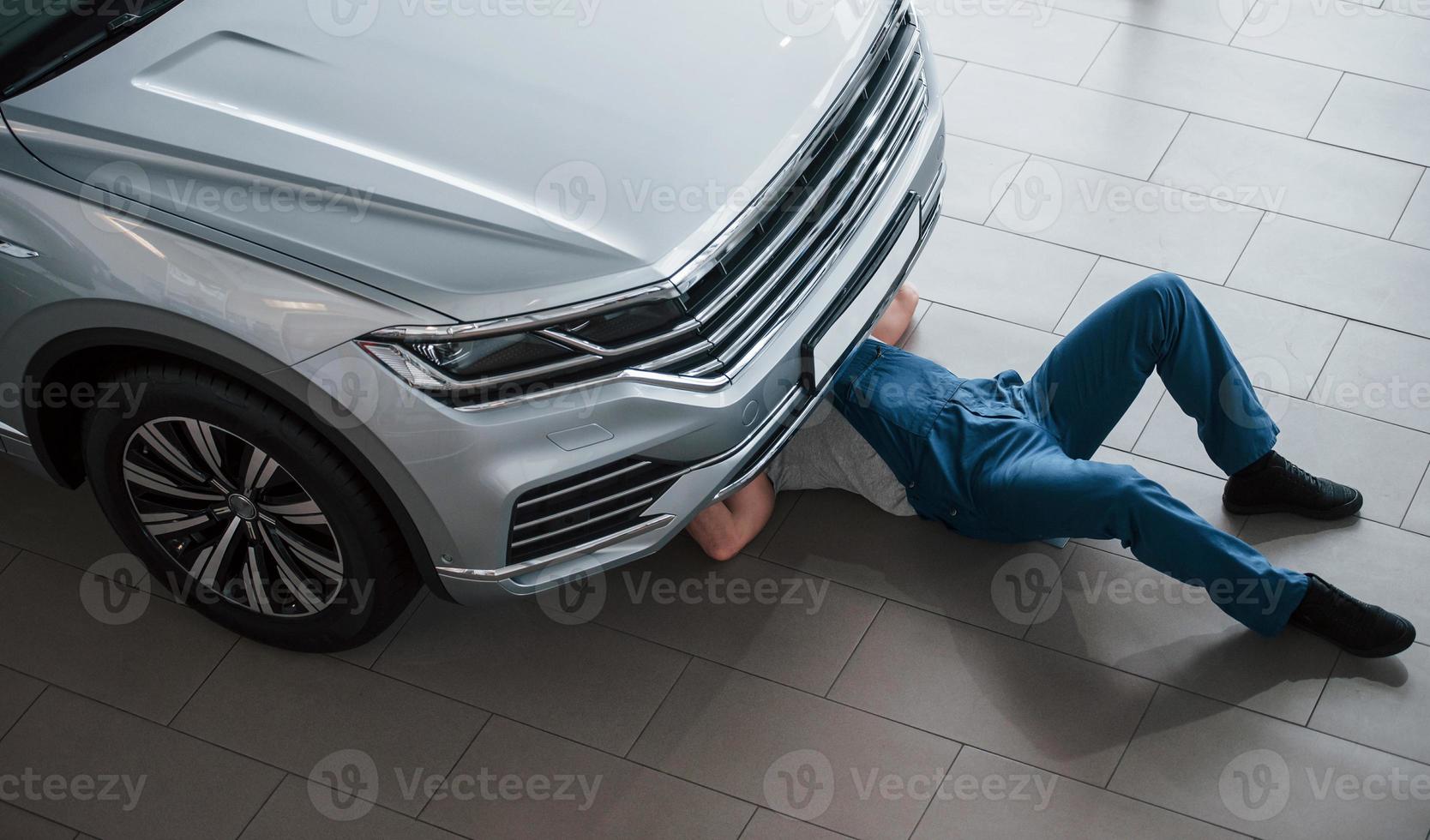 dans le garage. un homme en uniforme bleu travaille avec une voiture cassée. faire des réparations photo