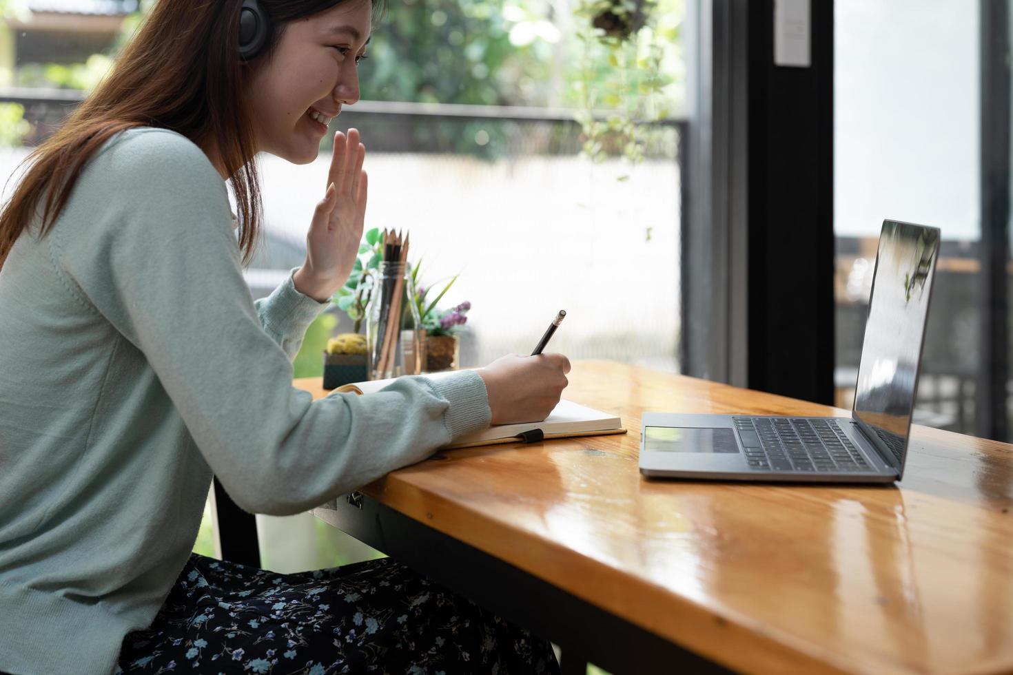 une étudiante souriante porte un casque sans fil étudie en ligne avec un enseignant, une jeune femme asiatique heureuse apprend la langue écoute une conférence regarde un webinaire écris des notes regarde un ordinateur portable assis dans un café, éducation à distance photo