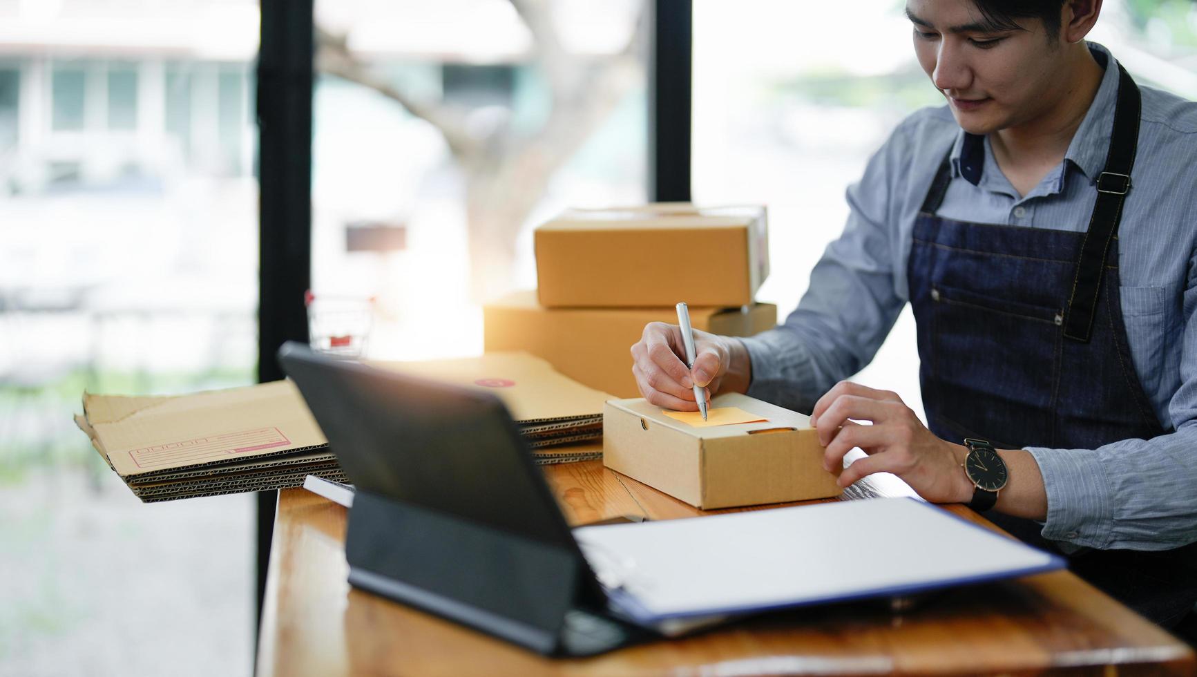 jeune entrepreneur PME homme indépendant utilisant un smartphone recevoir le client de la commande et prendre note de travailler avec l'emballage trier la livraison du marché en ligne de la boîte sur le bon de commande et préparer le produit de l'emballage photo